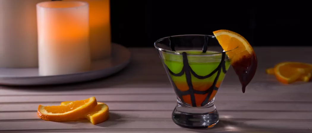 Chocolate web drawn in a glass of Spider's Kiss garnished with a chocolate-dipped orange slice alongside with some orange slices.