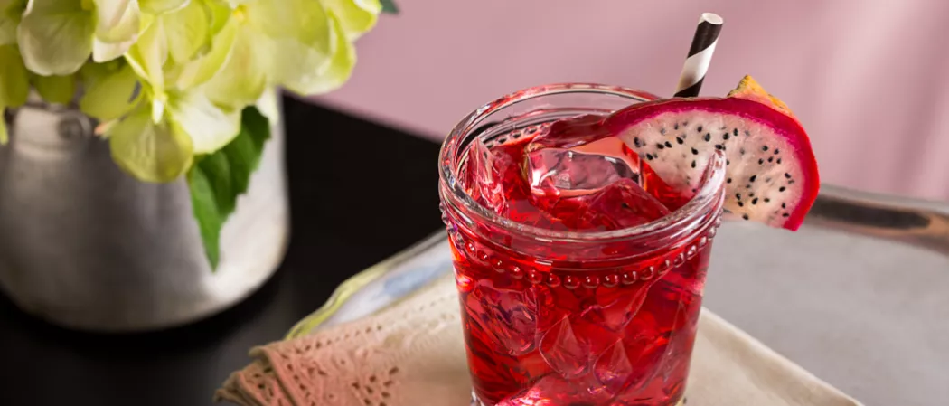  A glass of Paris Dream garnished with slice of dragon fruit and a straw, placed on a wooden surface