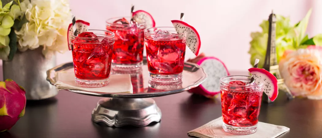 Four  glasses of Paris Dream garnished with slice of dragon fruit and  a straw,  three placed on a steel turntable