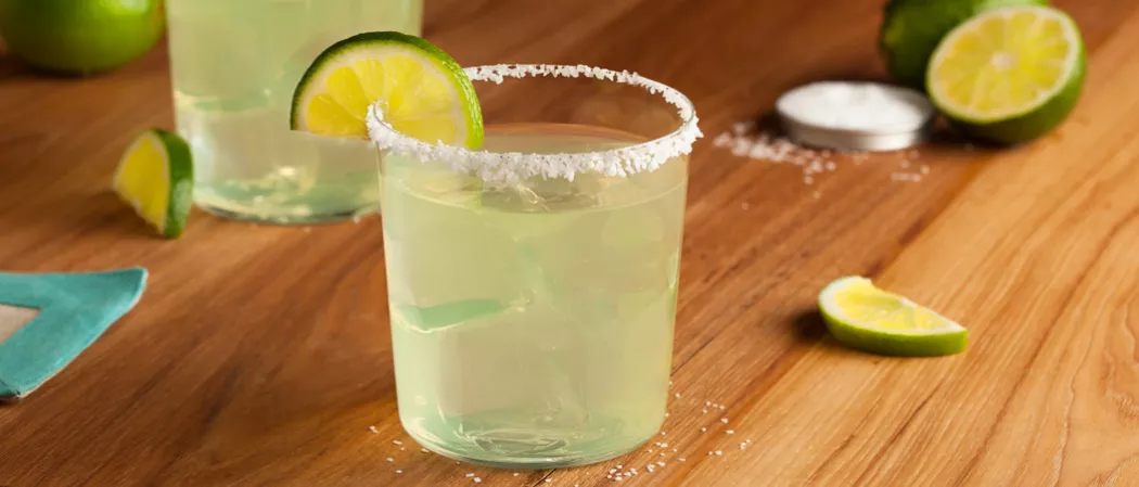 A glass of Premier Margarita and ice with a refreshing lemon wedge,