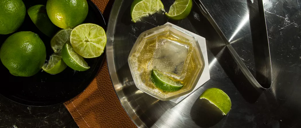 A glass of CC® Ginger Ale garnished with Lime Wedge along with chopped lemon in the plate on a table