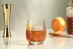 Glass of Legent® Blossom Old Fashioned alongside one jigger, one peeled orange and bottle of liquor